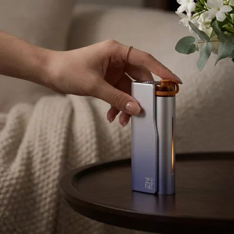 Zhithera D1 waterless diffuser: hand pressing the top of the silver-blue device on a round side table