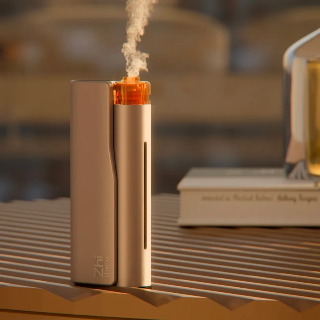 Gold Zhithera D1 waterless diffuser releasing a fine mist next to a book on a wooden shelf
