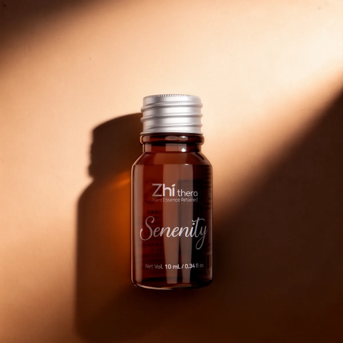 Zhithera 10 ml essential oil amber bottle labeled "Serenity" with silver cap in warm light