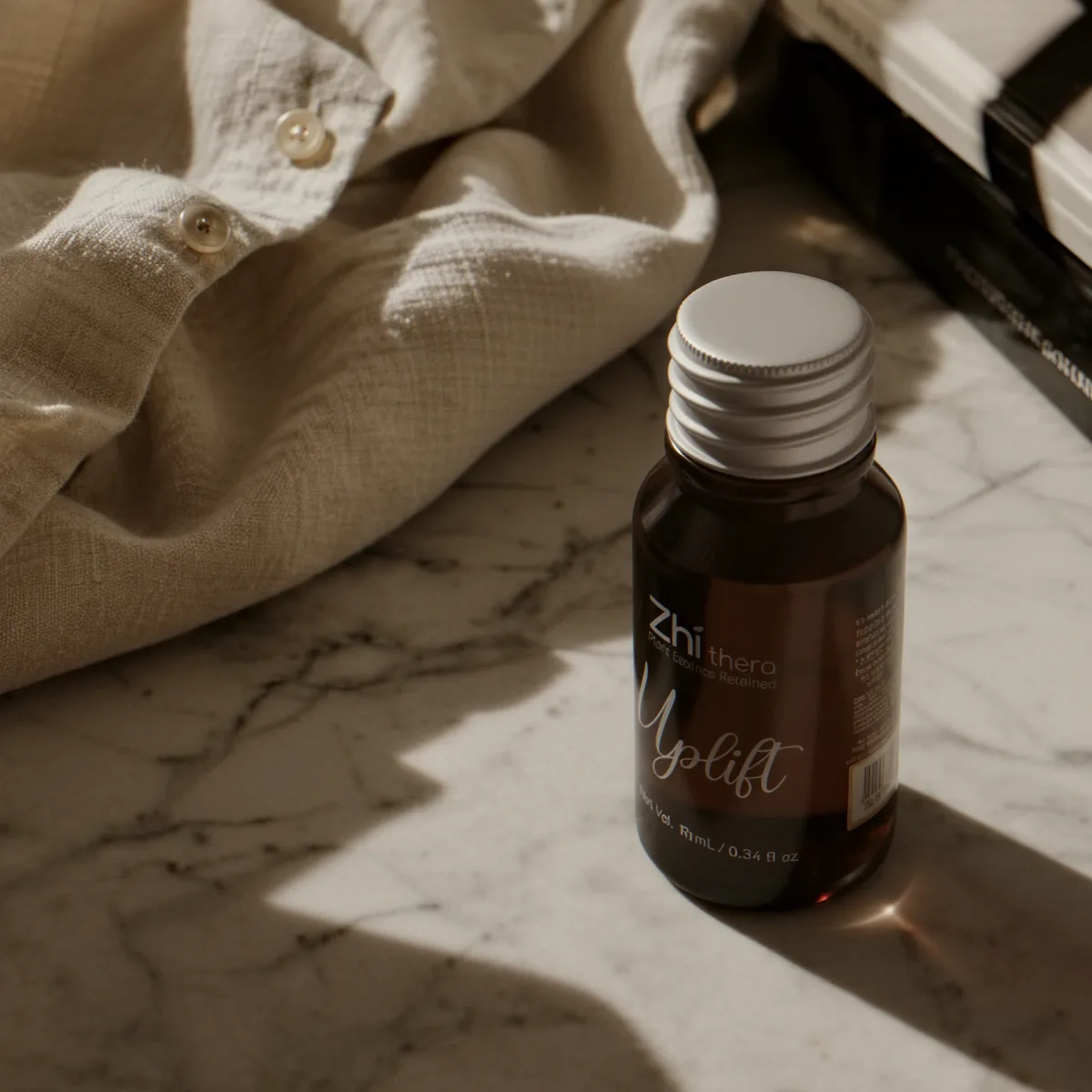 Zhithera 10 ml amber essential oil bottle labeled "Uplift" on white marble beside linen