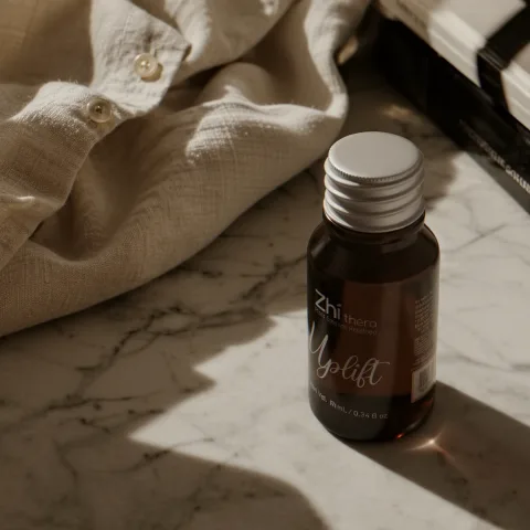 Zhithera 10 ml amber essential oil bottle labeled "Uplift" on white marble beside linen