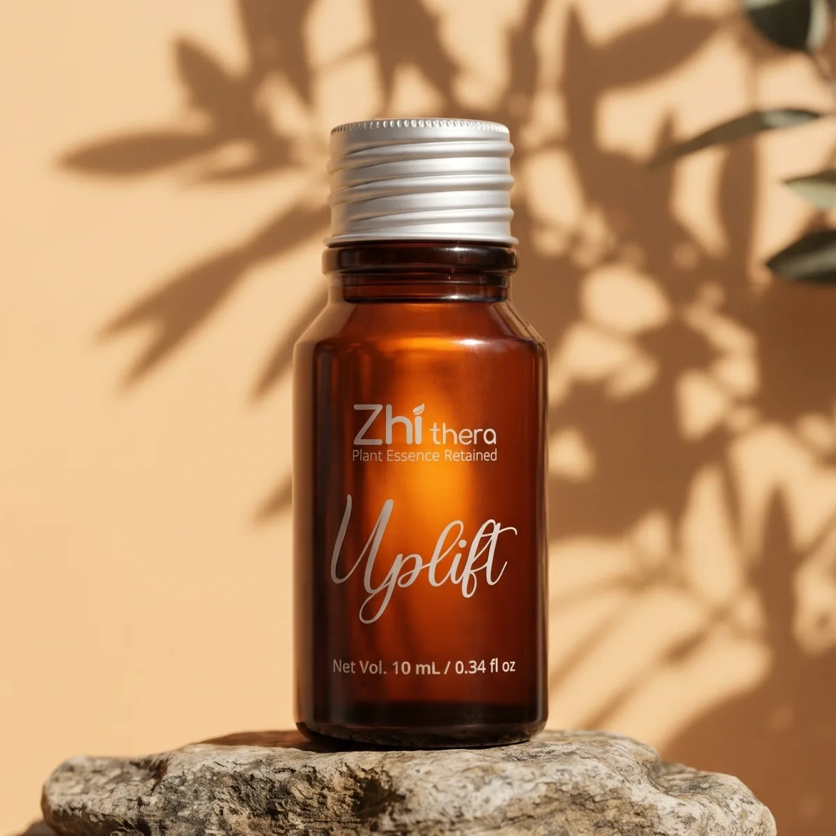 Zhithera 10 ml amber glass essential oil bottle labeled "Uplift" on a rock with leaf shadows