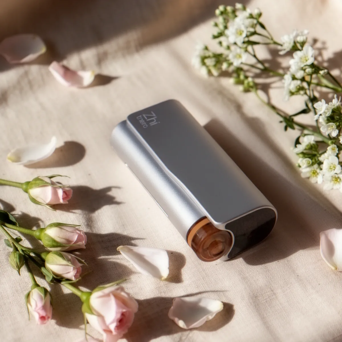 Silver Zhithera D1 cordless waterless diffuser on a cream tablecloth with small pink roses