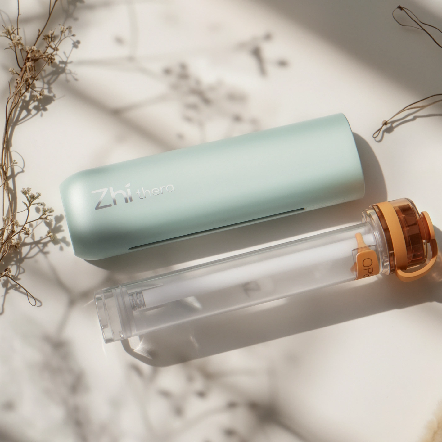 A mint-green cylindrical Zhi thero diffuser case and a clear refill tube with orange accents lie on a bright white surface…