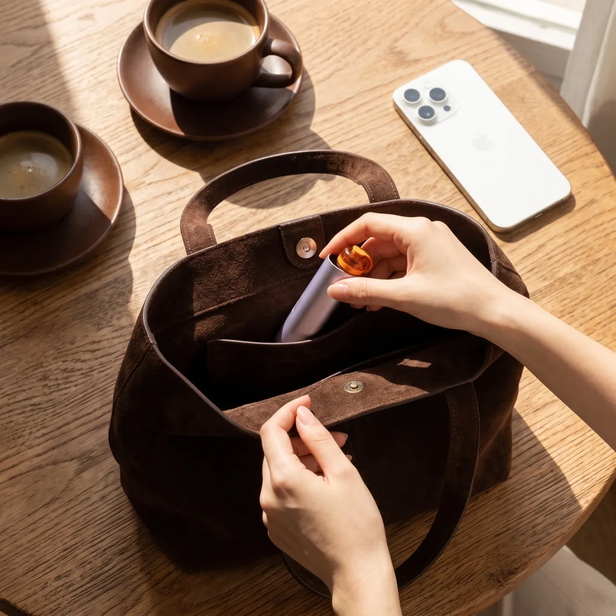 Hand taking the Zhithera D1 Mini car diffuser out of a dark tote beside a coffee and phone