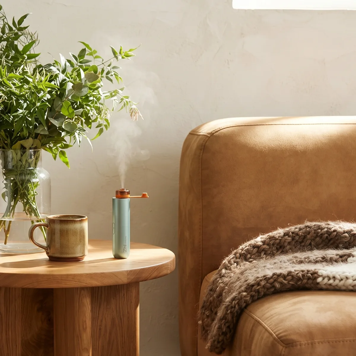 Mint Zhithera D1 Mini diffuser misting on a side table by a leather armchair and plant