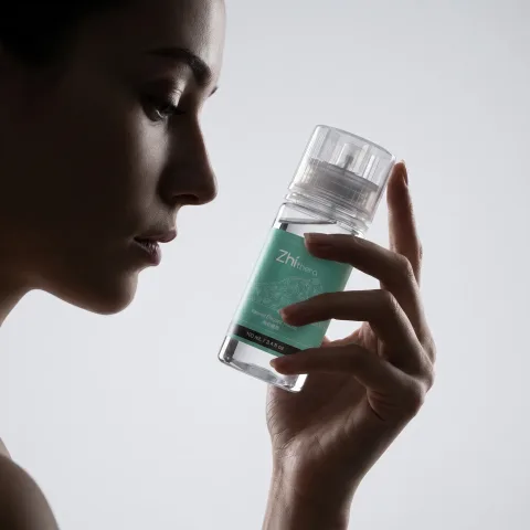 Profile of a woman holding a teal-label Zhithera 100 ml fragrance oil bottle