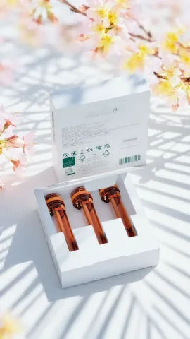 Open box of three Zhithera refillable cartridges with amber caps in dappled light